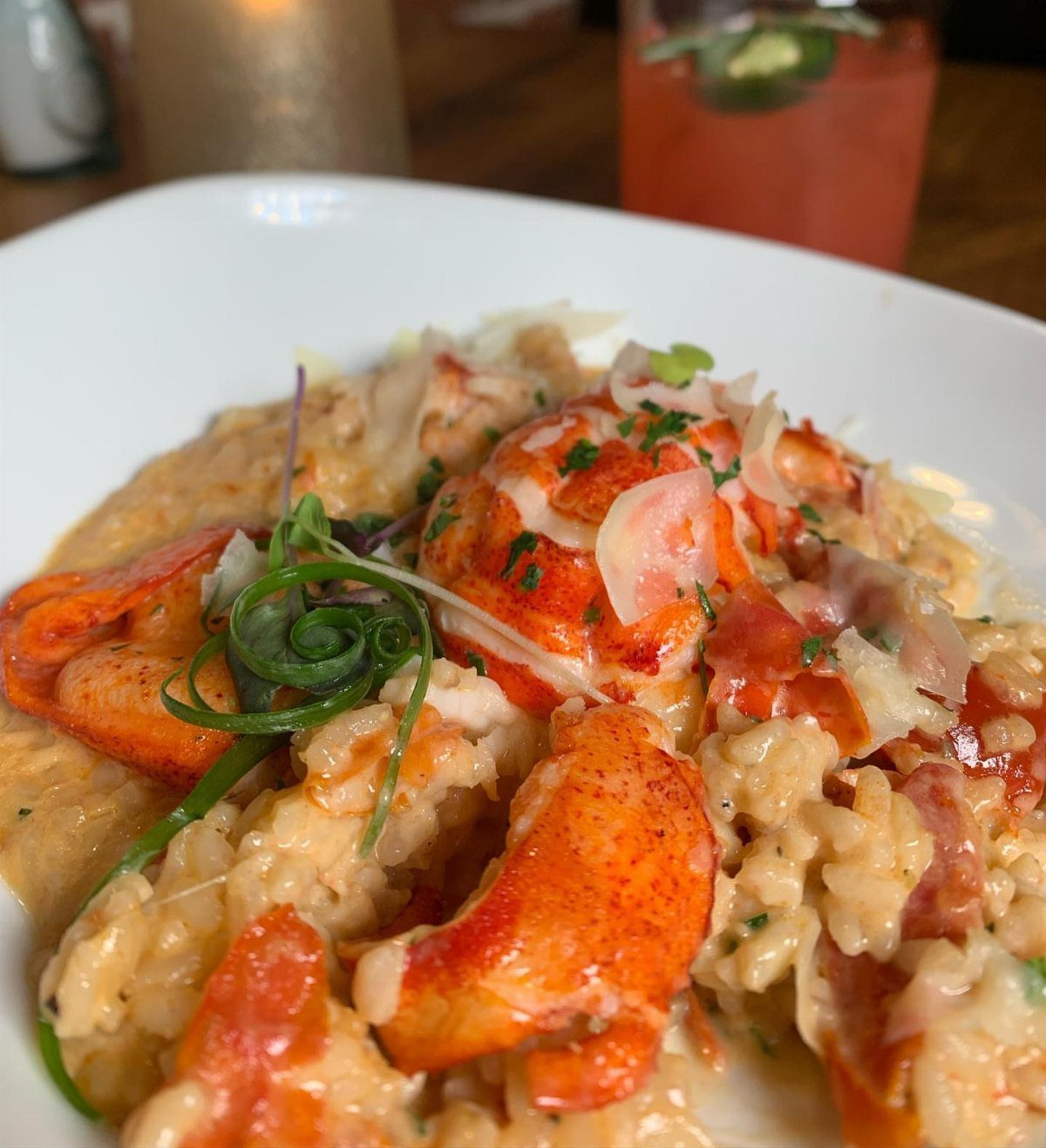 Creamy lobster risotto in a white bowl garnished with fresh green herbs.