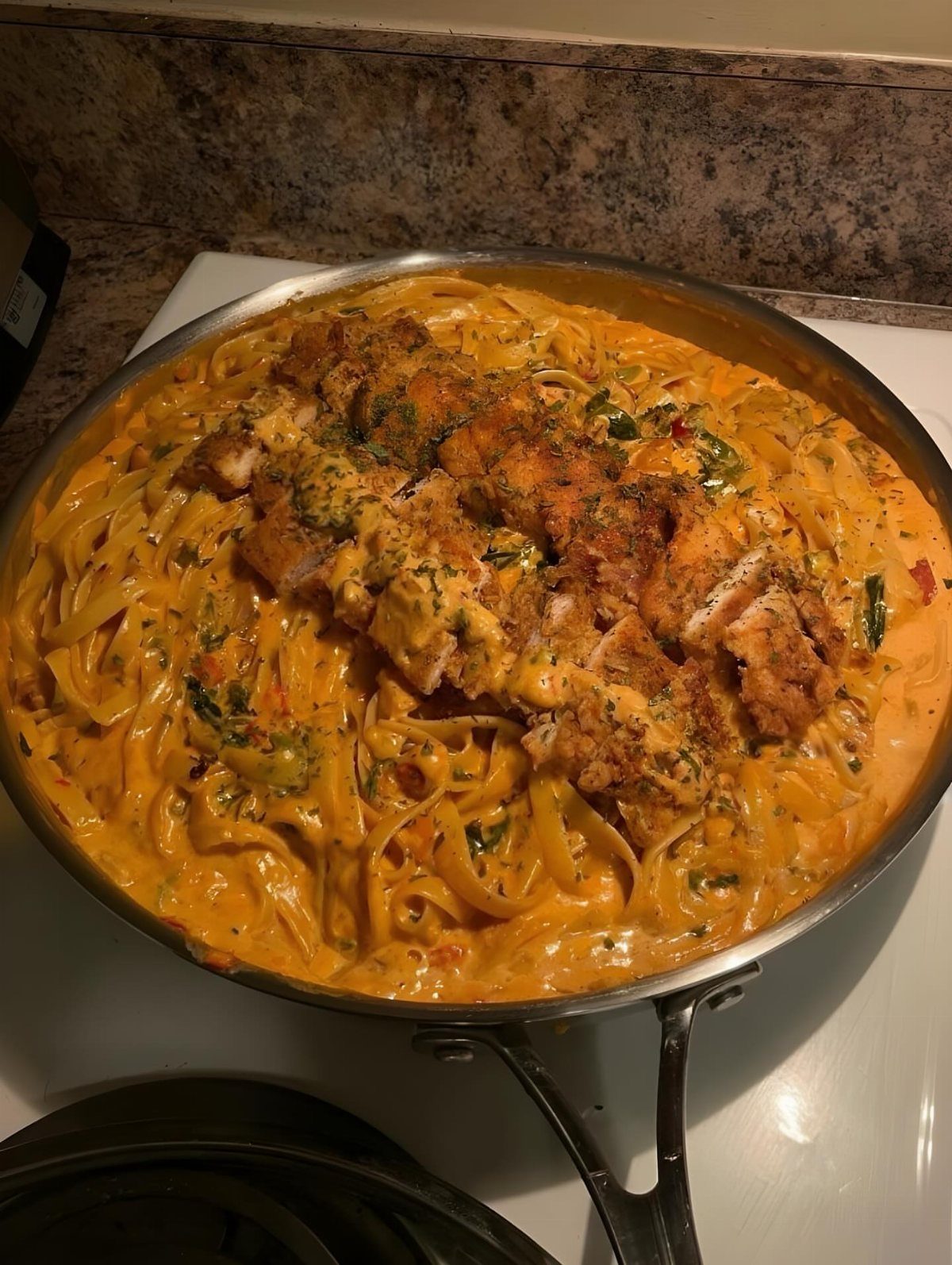 Creamy chicken and pasta dish in a stainless steel skillet with fresh herbs.