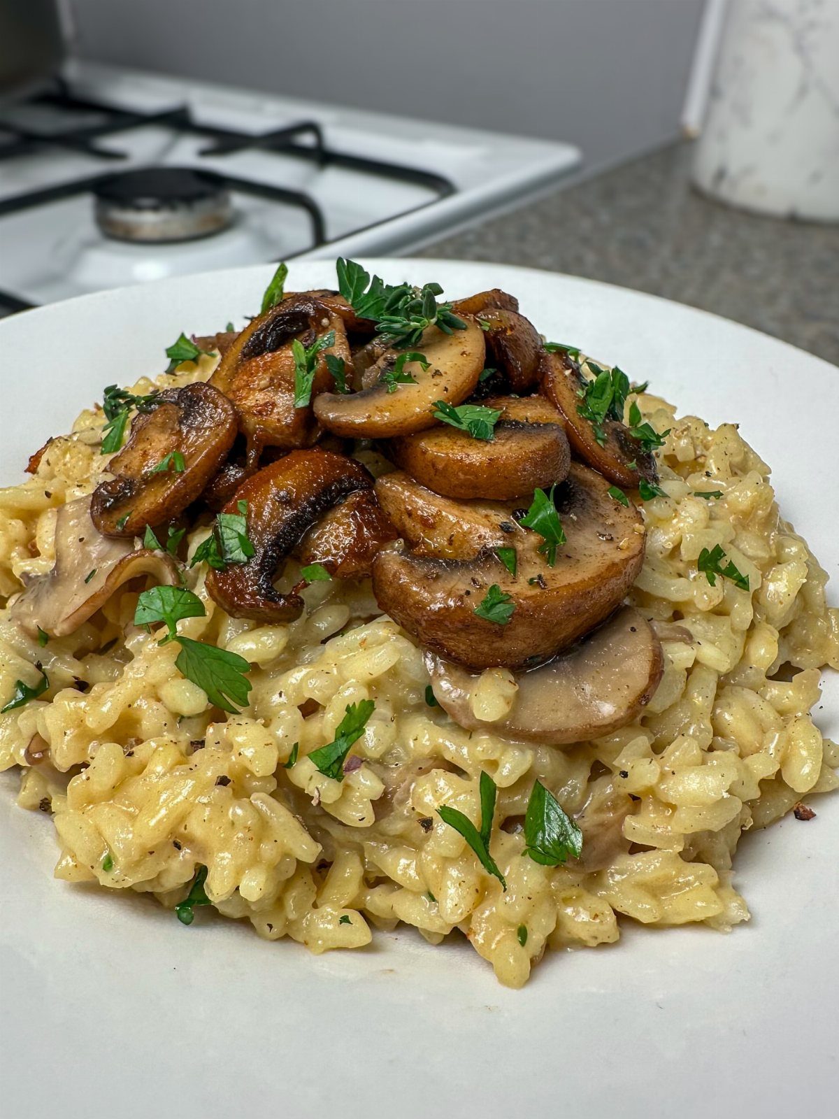 Creamy mushroom risotto topped with sautéed mushrooms and fresh parsley on a white plate.