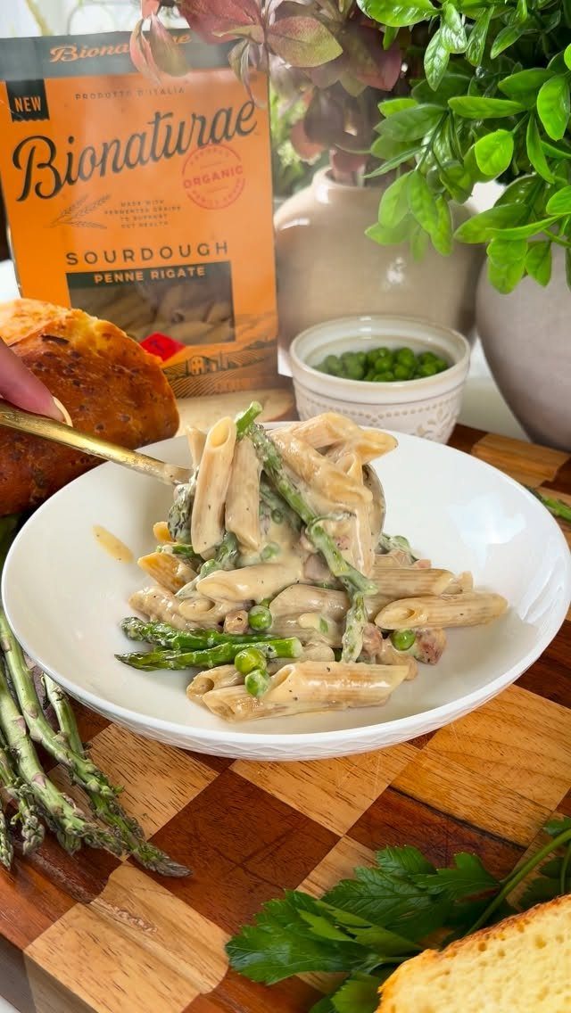 Penne pasta with creamy sauce, asparagus, and peas in a white bowl.