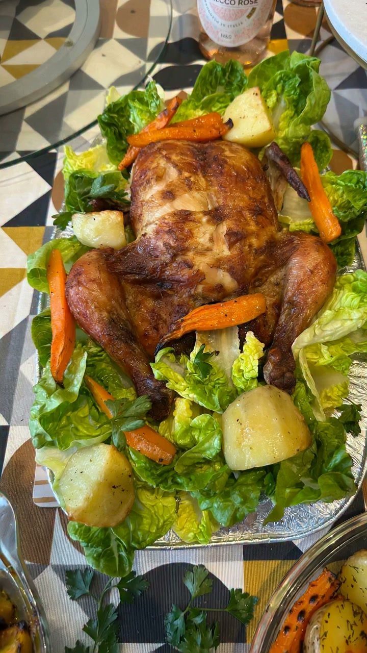 Whole roasted chicken with carrots and potatoes on a bed of lettuce leaves.
