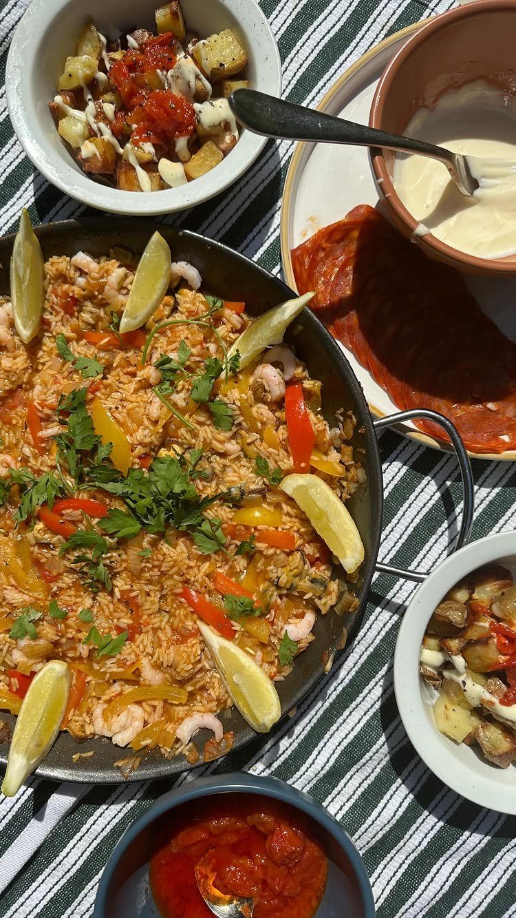 Seafood paella with shrimp and peppers in a pan on a striped tablecloth.