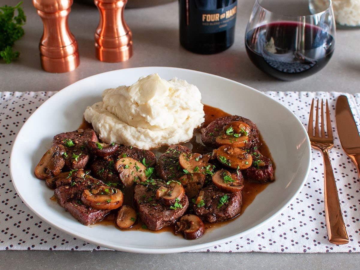 Steak medallions with mushroom sauce and mashed potatoes served with red wine.