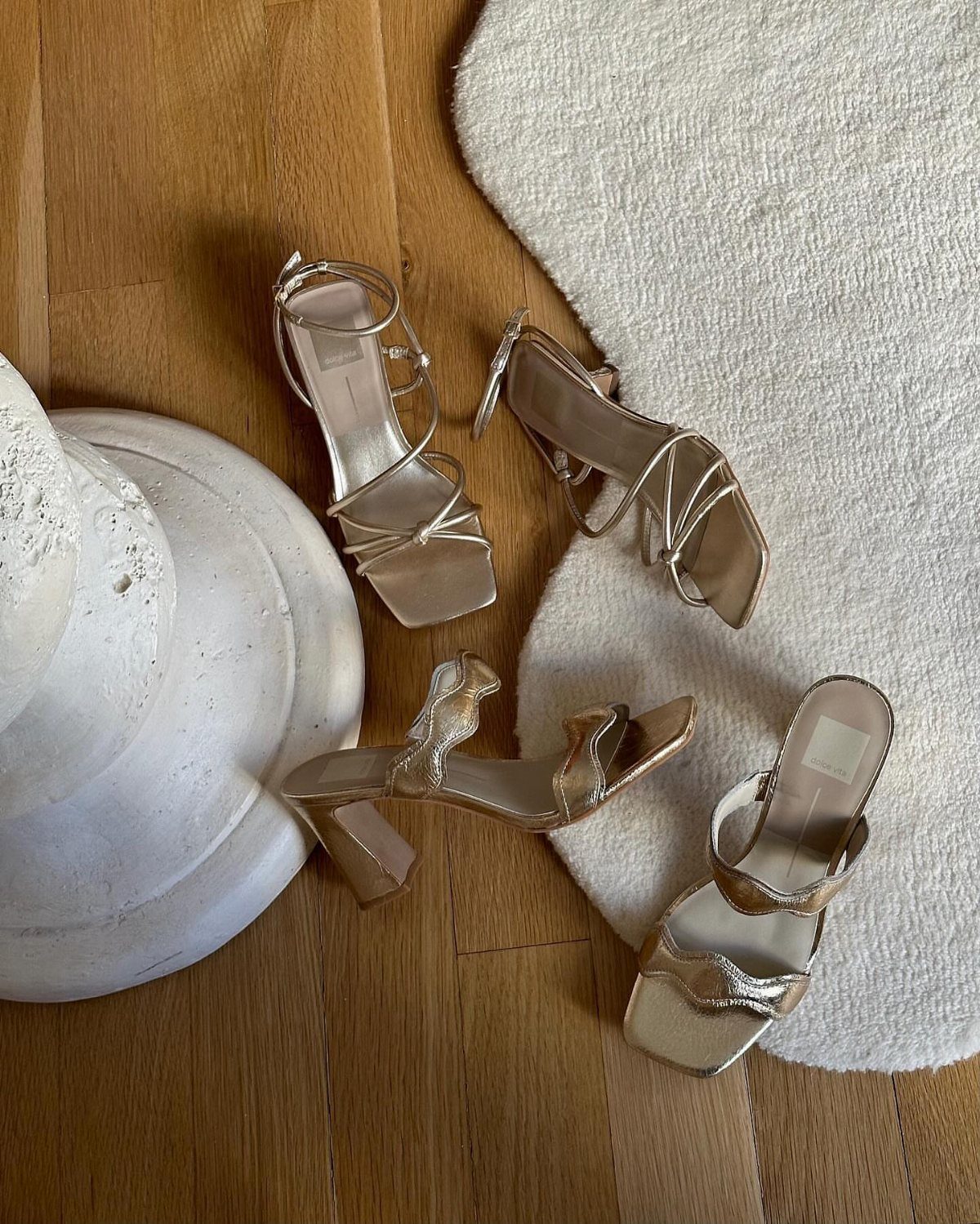 Beige high-heeled sandals arranged on a wooden floor and white textured rug.
