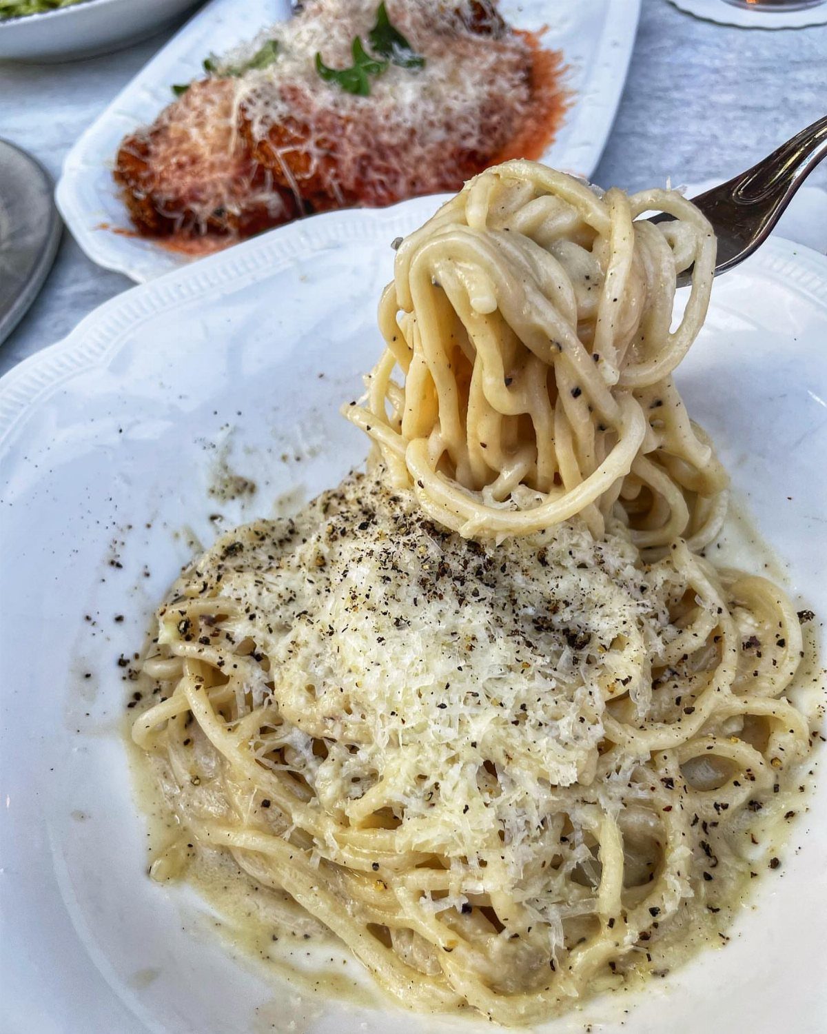 Creamy spaghetti pasta with black pepper and cheese being lifted by a fork.