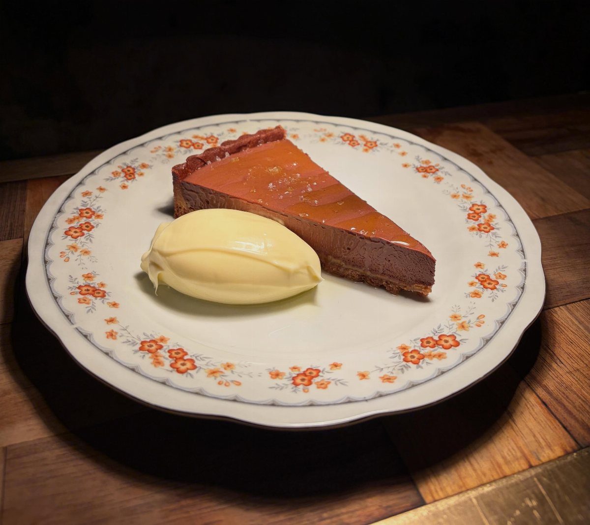Chocolate and caramel tart slice with vanilla ice cream on a floral plate.