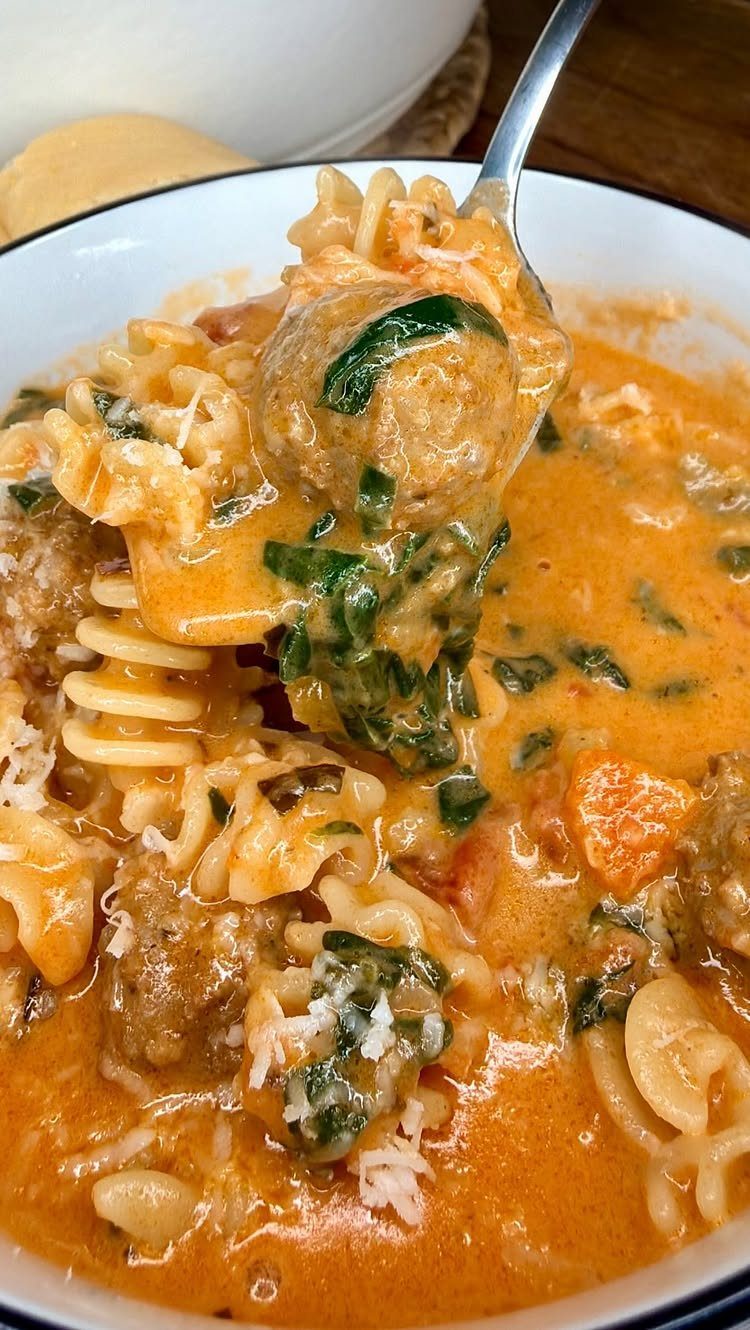 Creamy meatball soup with rotini pasta and spinach being lifted by a spoon.