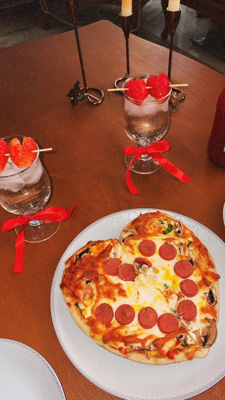Heart-shaped pepperoni pizza on a white plate with strawberry drinks and candles.