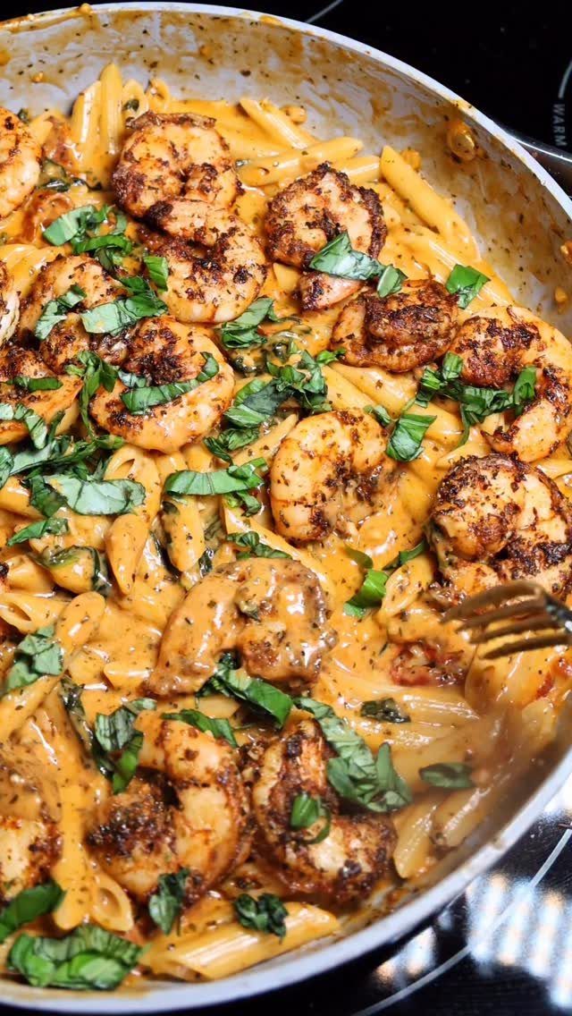 Penne pasta with creamy sauce, seared shrimp, and fresh basil in a pan.