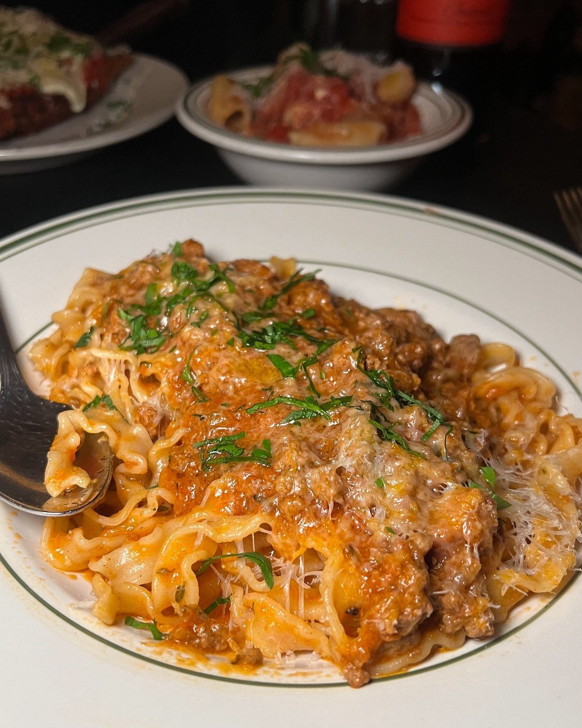 Wide ribbon pasta topped with meat ragu, melted cheese, and fresh parsley.