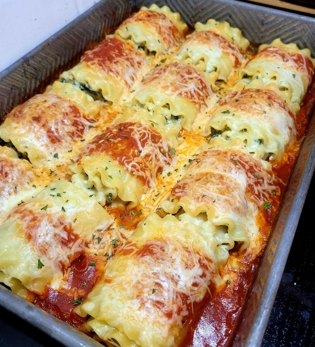 Lasagna roll-ups with melted cheese and tomato sauce in a baking pan.