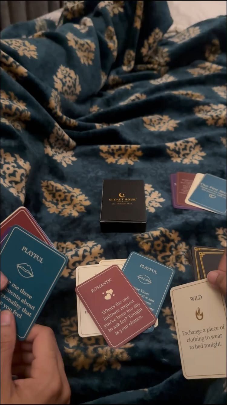 Game cards with romantic and playful prompts held over a blue patterned blanket.
