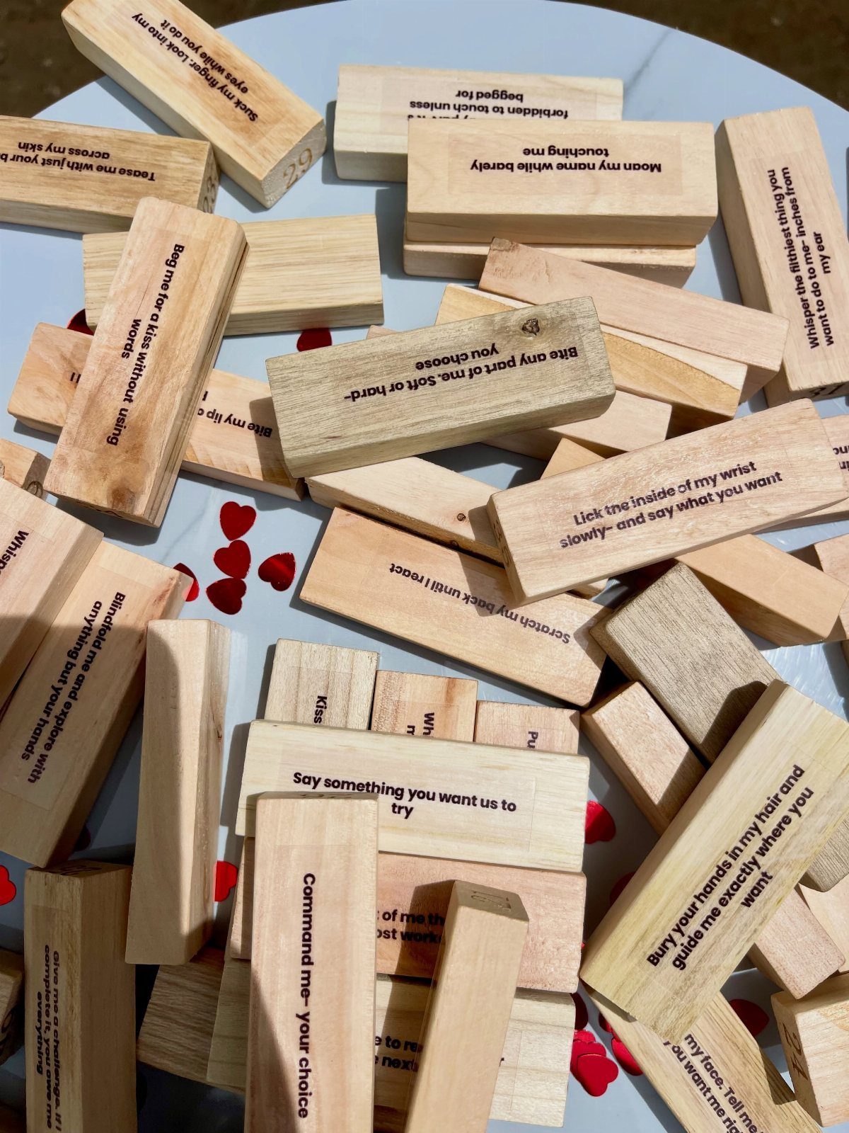 Wooden blocks with printed romantic dares scattered on a blue surface with red hearts.