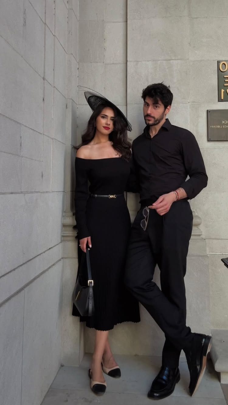 Man in black button-up shirt and trousers posing with woman in black dress.