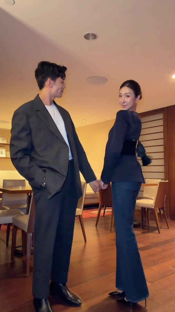 Man in grey blazer and white t-shirt holding hands with a woman.