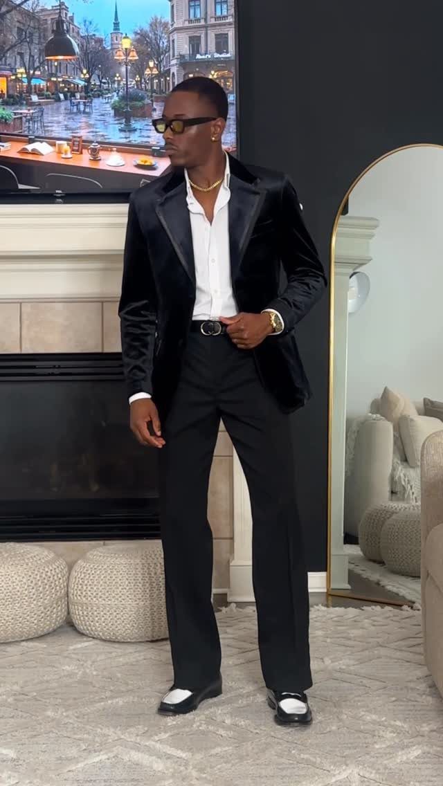 Man in a black velvet blazer and white shirt posing in a living room