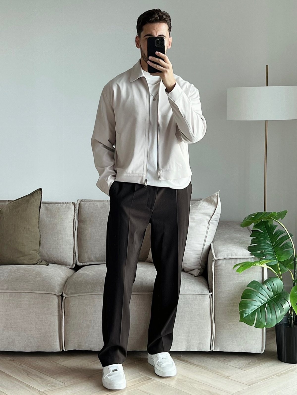 Man wearing a beige jacket and dark trousers posing for a mirror selfie.