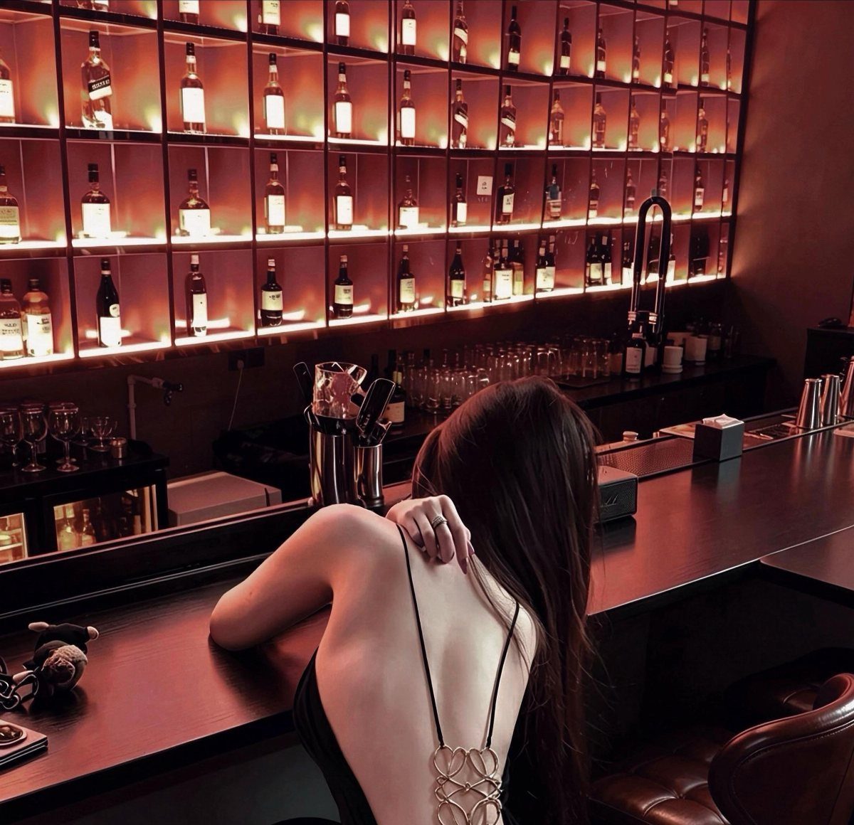 Woman in a black backless dress sitting at a dimly lit cocktail bar.