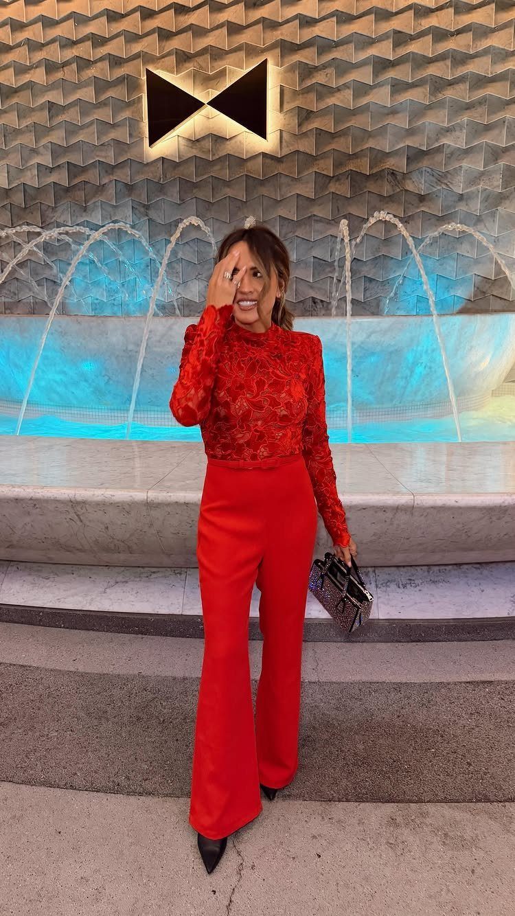 Woman in red lace top and wide-leg trousers standing by a fountain