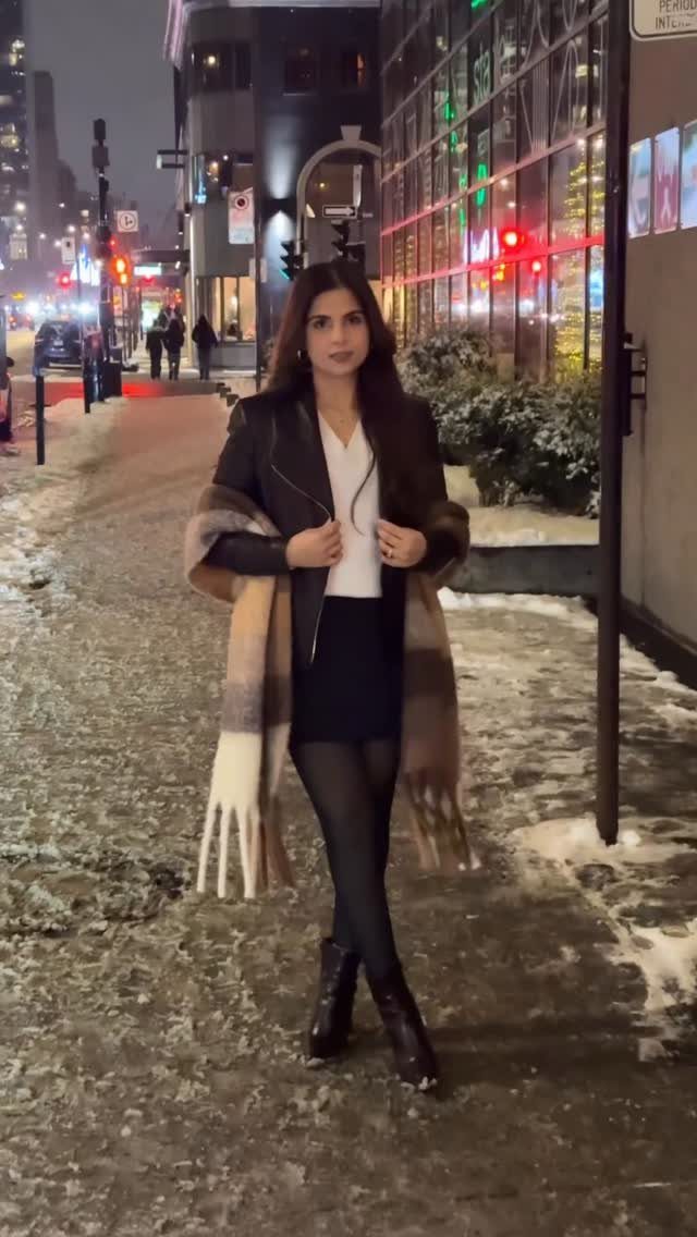 Woman wearing a black leather jacket and plaid scarf on a snowy city street.