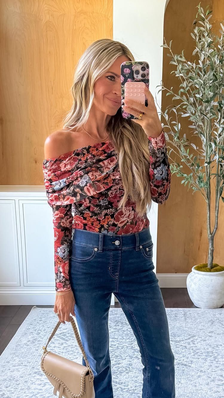 Woman wearing a floral off-the-shoulder statement shirt and dark blue jeans.