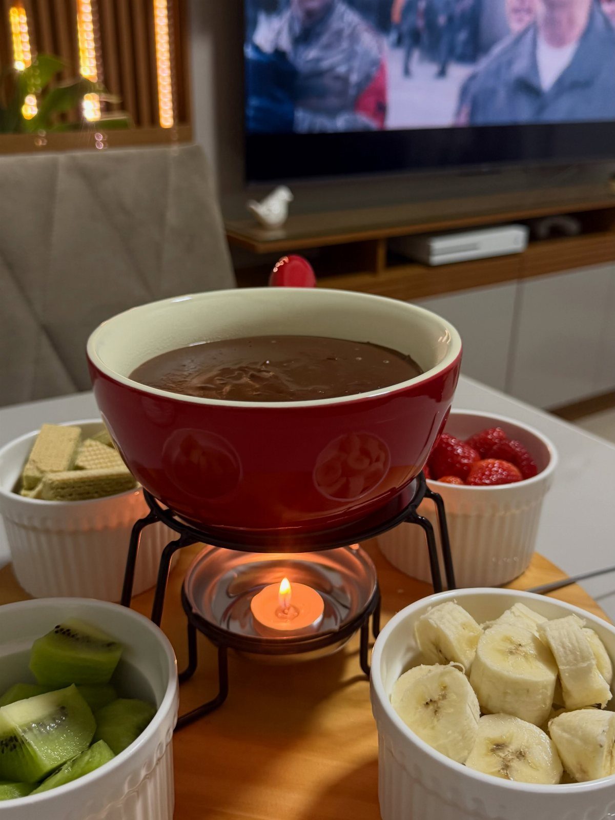 Chocolate fondue pot with a lit candle surrounded by bowls of fresh fruit.