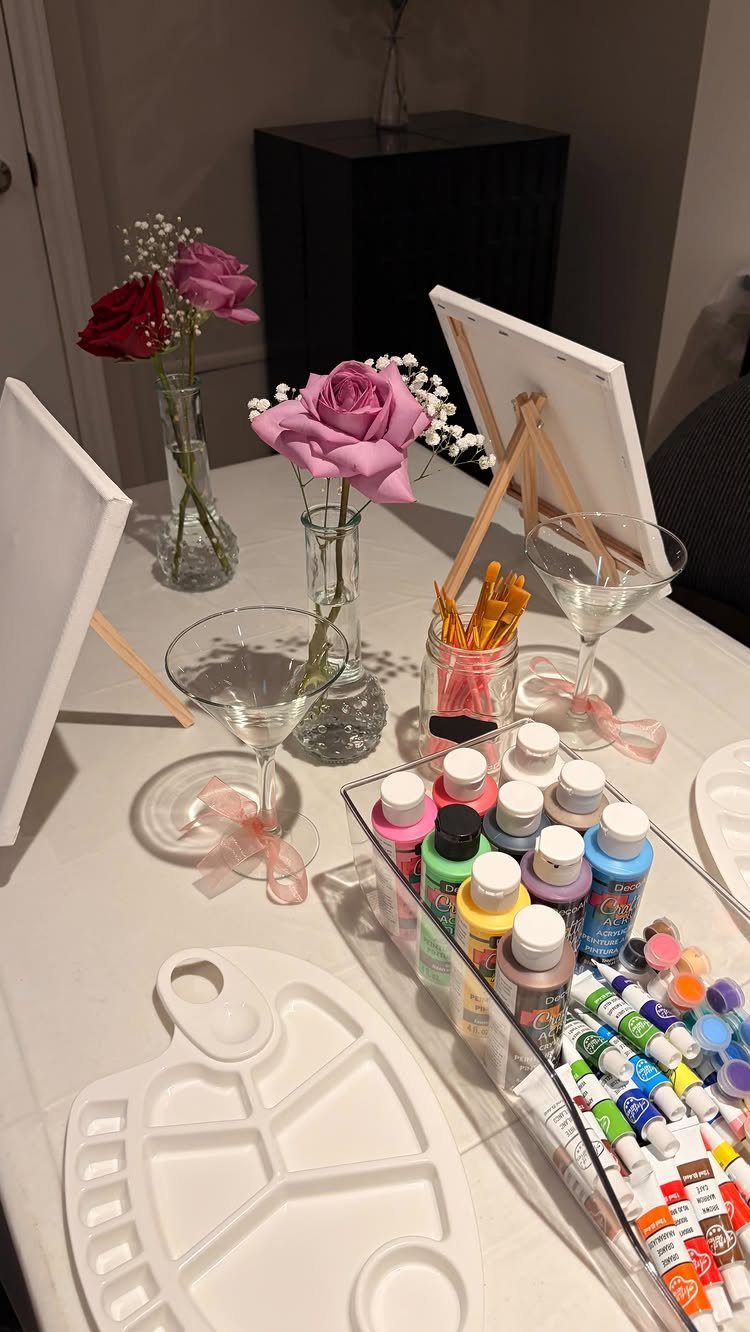 Painting supplies and martini glasses on a table with pink and red roses.