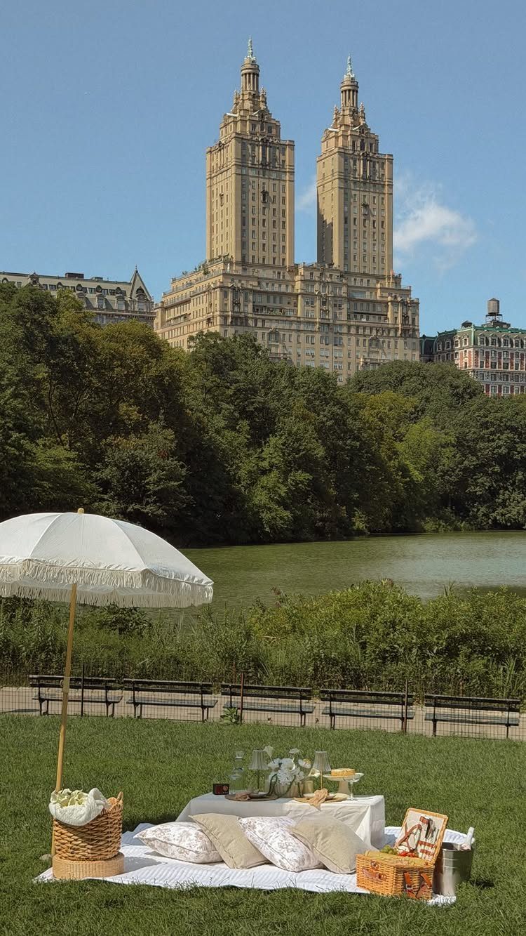 Picnic setup with white blanket and umbrella overlooking a lake and city skyline.