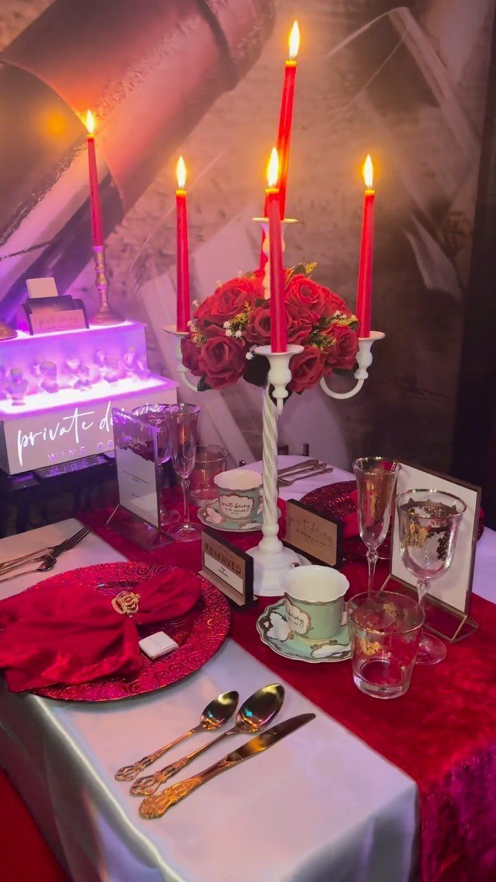 Romantic table setting with red velvet cloth, lit red candles, and gold cutlery.