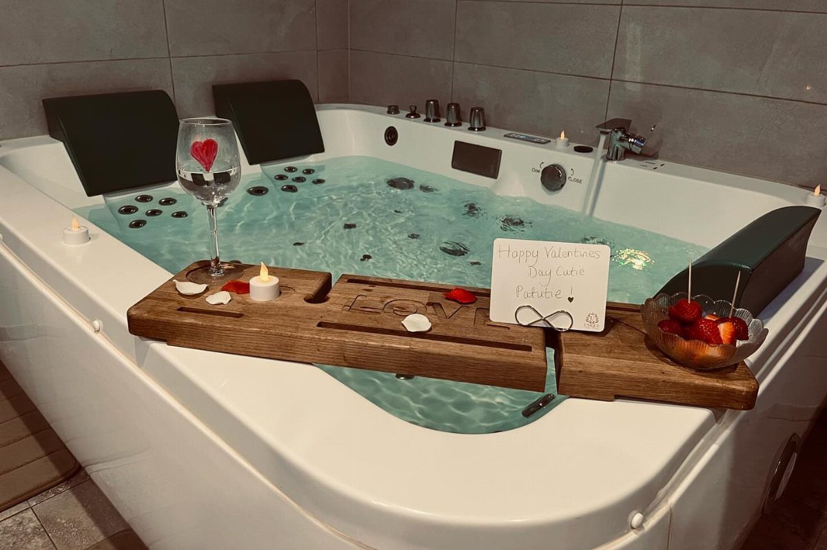 White jetted hot tub with a wooden tray holding strawberries, candles, and a note.