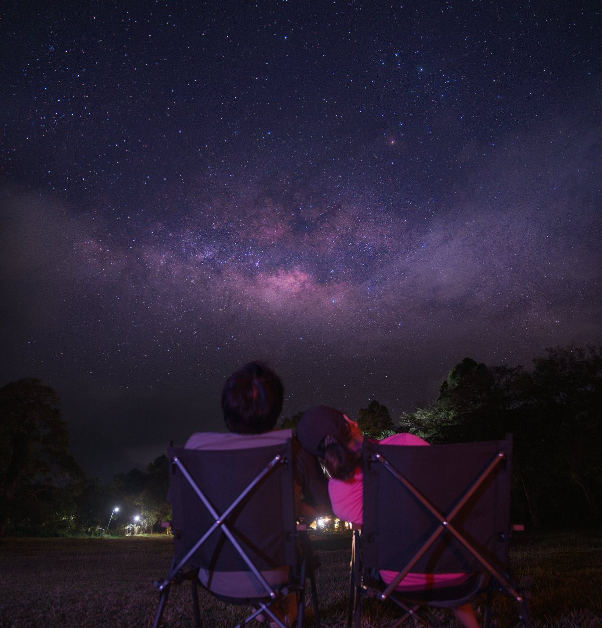 Two people sitting in chairs gazing at the starry Milky Way galaxy sky.