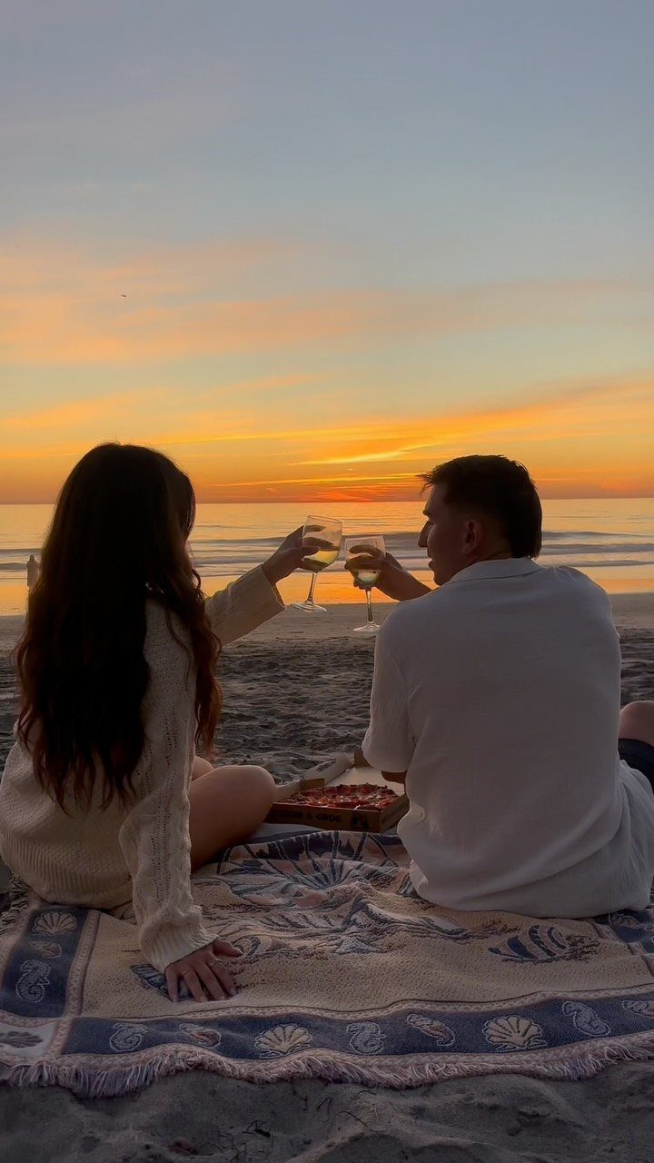 Couple clinking wine glasses during a romantic beach picnic at sunset