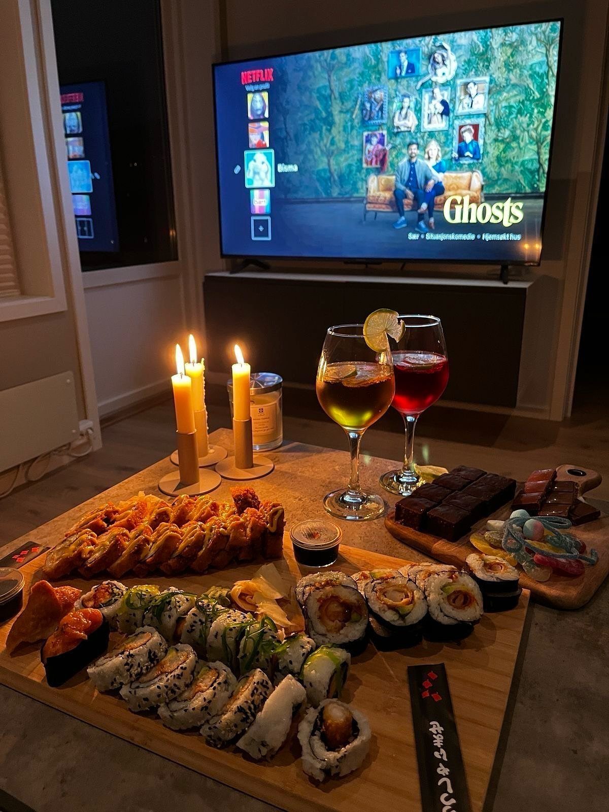 Sushi platter and cocktails on a wooden board with candles and a television.