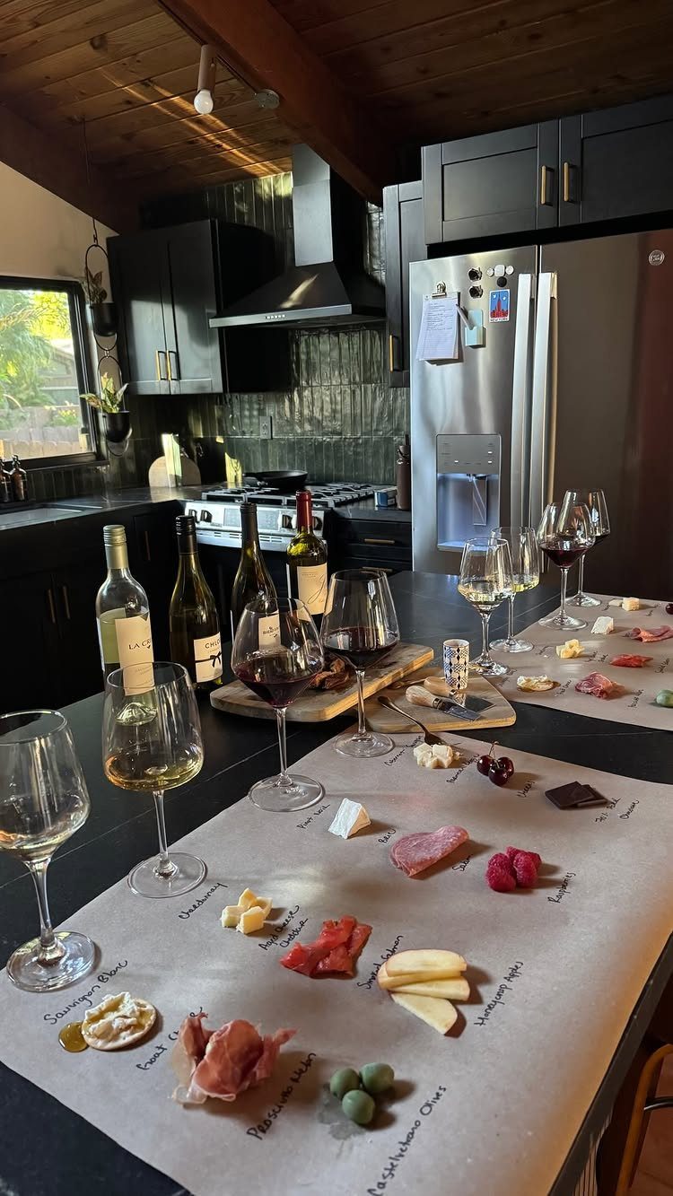 Wine bottles and glasses with a curated cheese and charcuterie board on parchment paper.