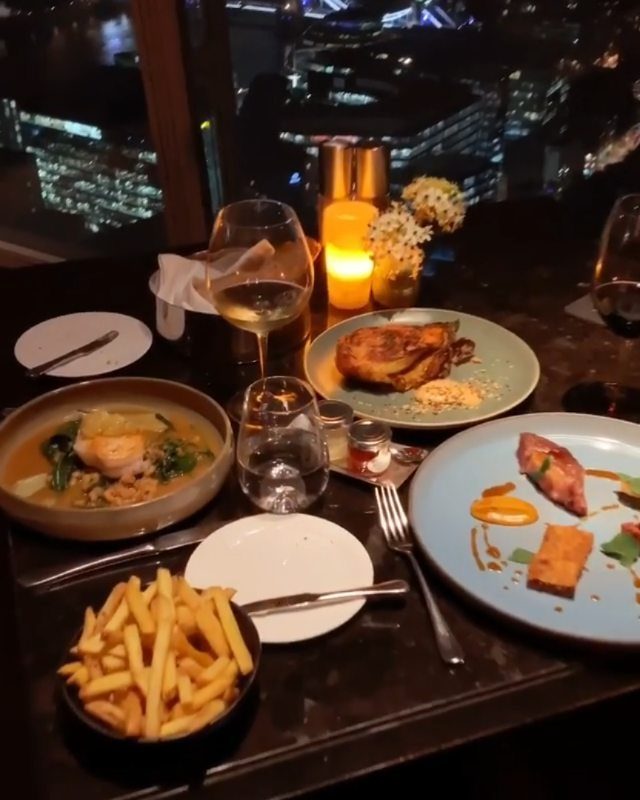 Gourmet dinner plates and wine glasses on a table overlooking a city skyline.