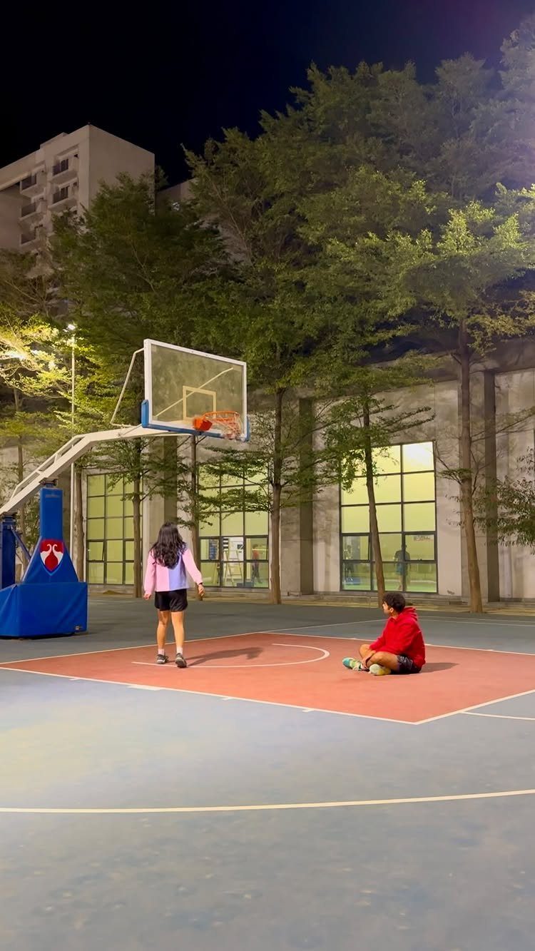 Two people spending time together on an outdoor basketball court at night.