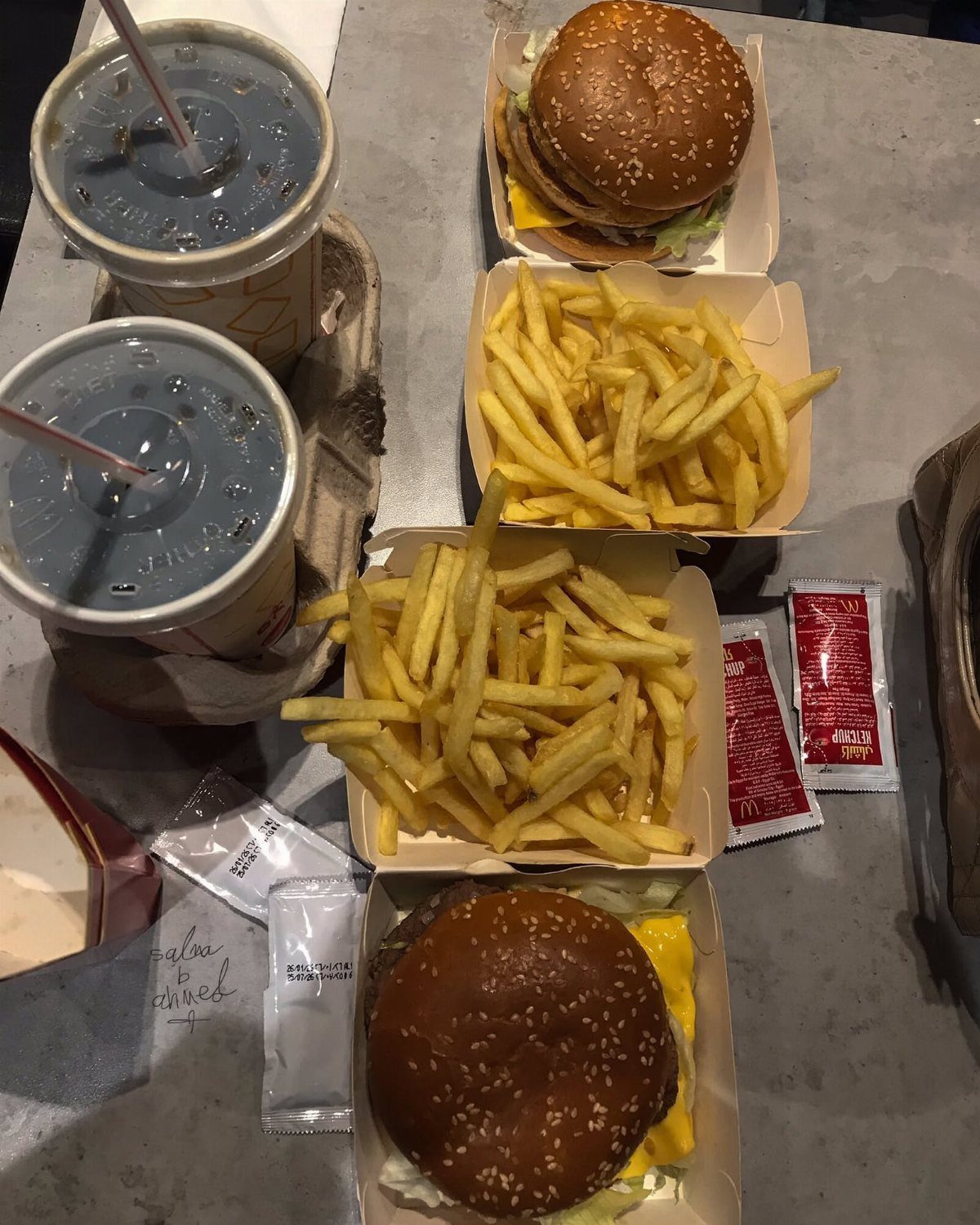 Two cheeseburgers, french fries, and iced drinks served in fast food packaging.