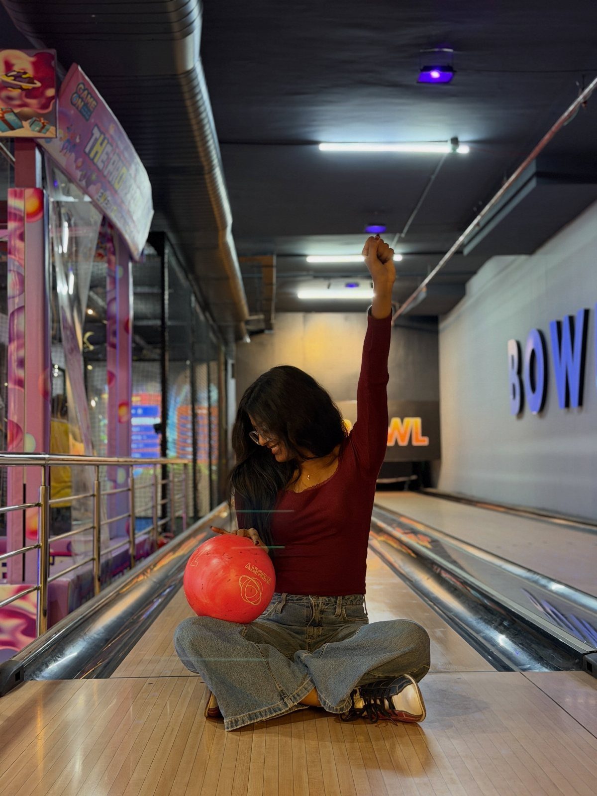 Woman sitting on a bowling lane holding a pink ball and celebrating victory.