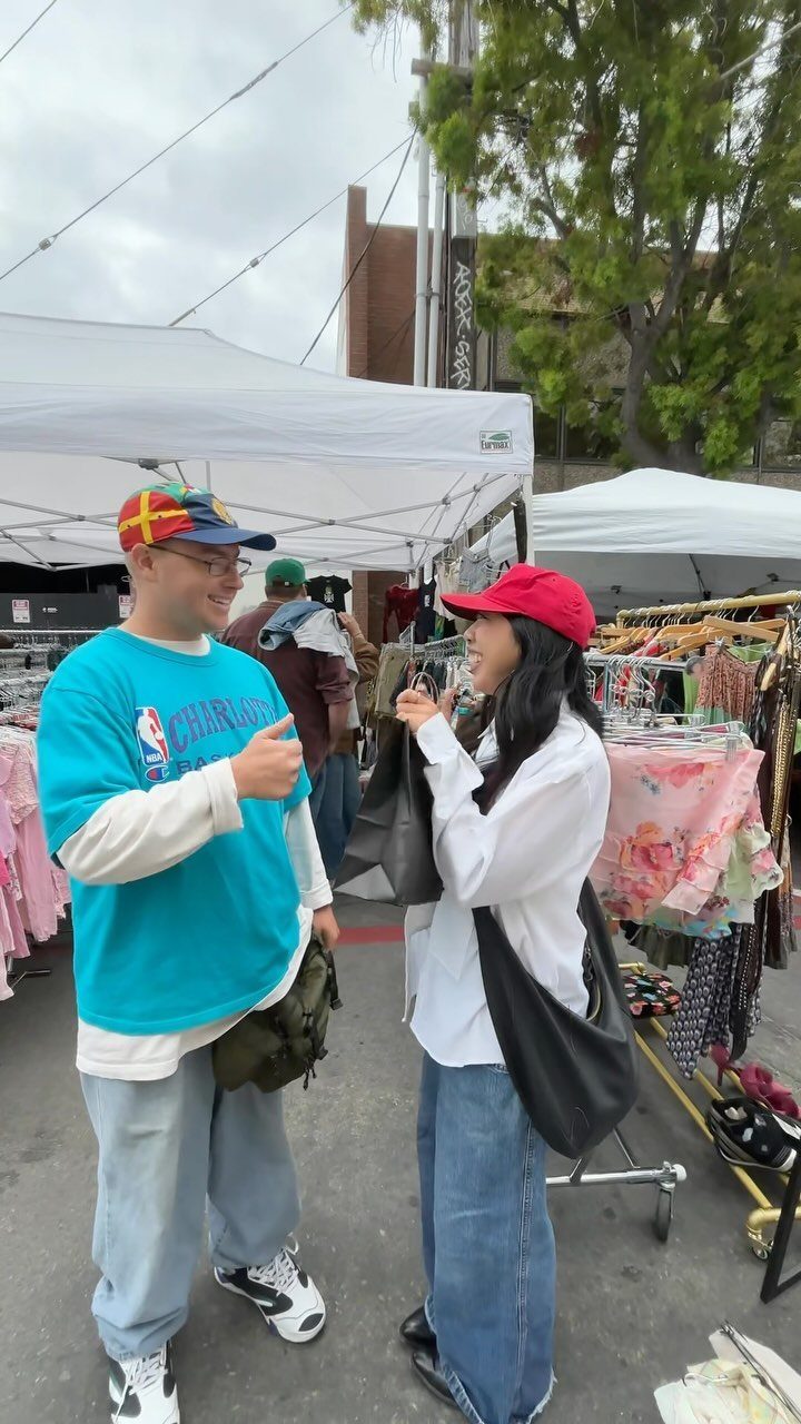 Couple talking while browsing clothing racks at an outdoor flea market with tents.