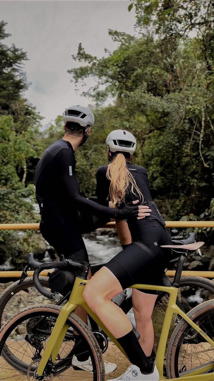 Couple in cycling gear standing by a yellow bike near a forest river