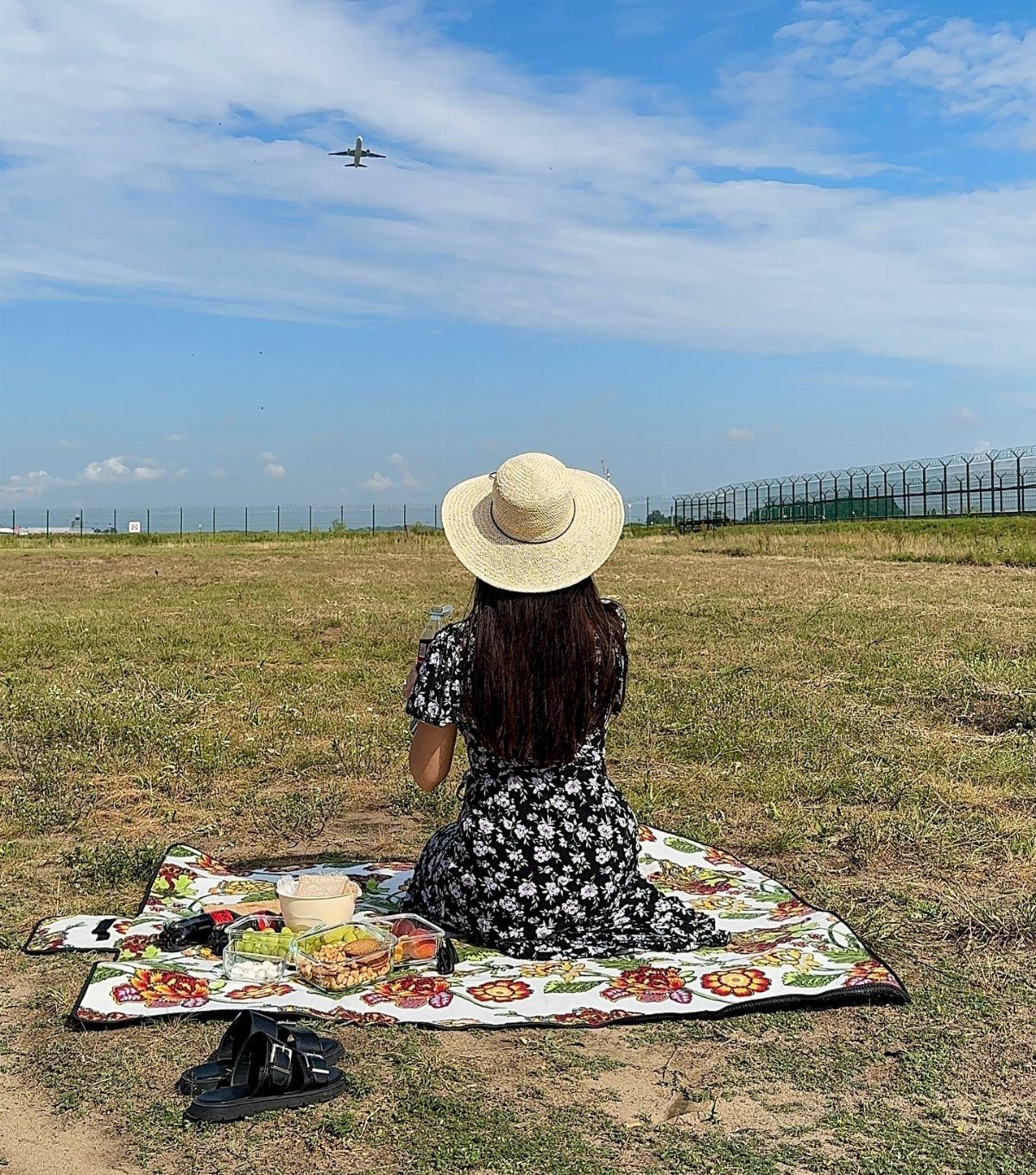 Woman in floral dress picnicking in a field watching a plane fly overhead