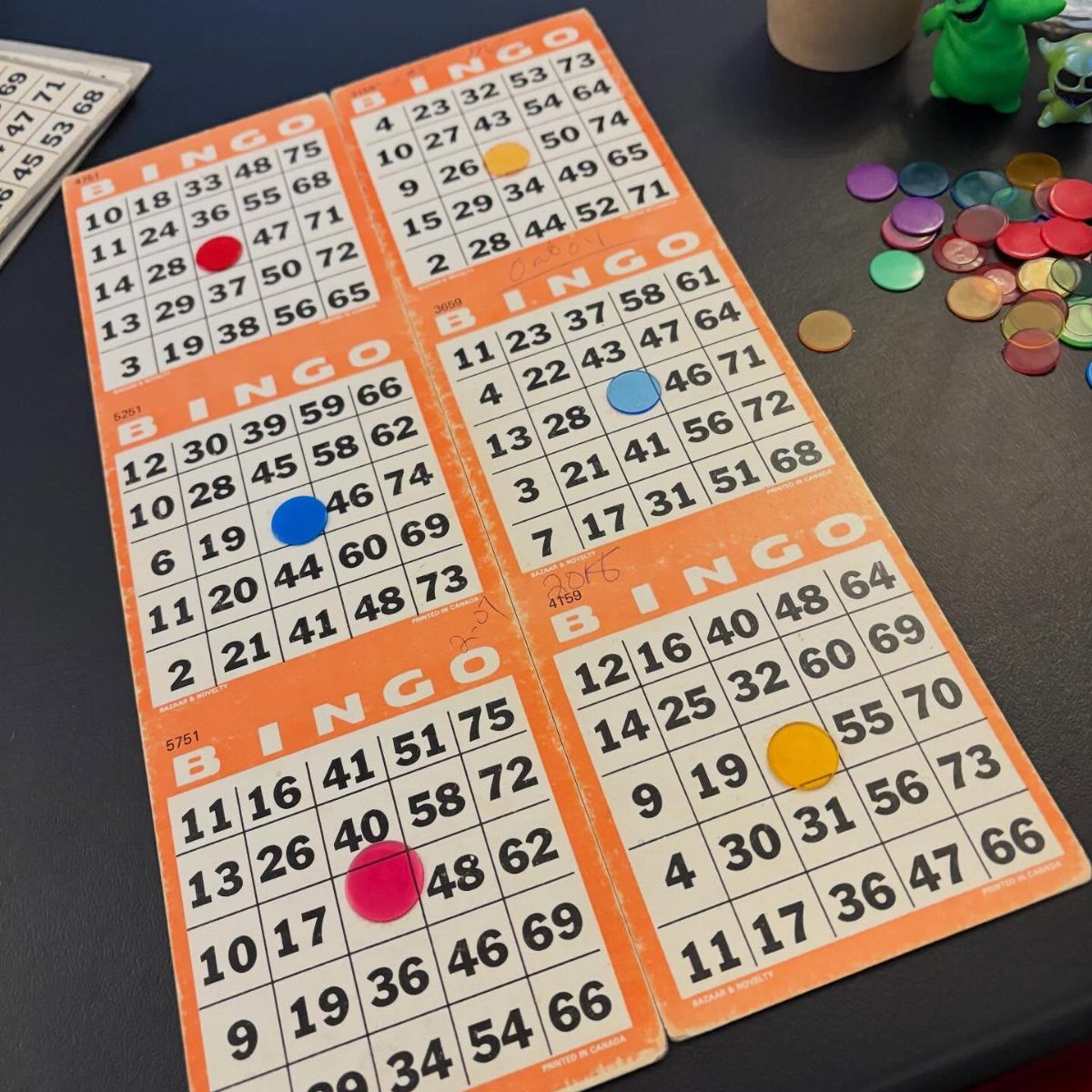 Bingo cards with colorful markers on a dark blue table for a game.
