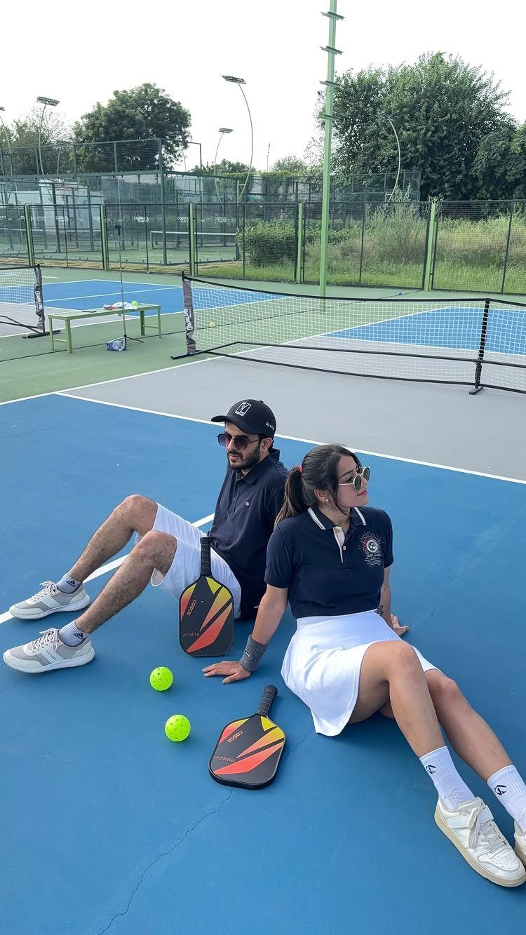 Couple sitting on a blue pickleball court with paddles and yellow balls.