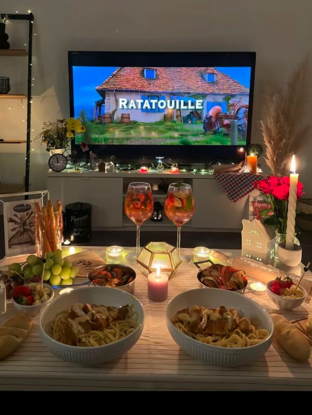 Dinner table with pasta and wine in front of a TV playing Ratatouille