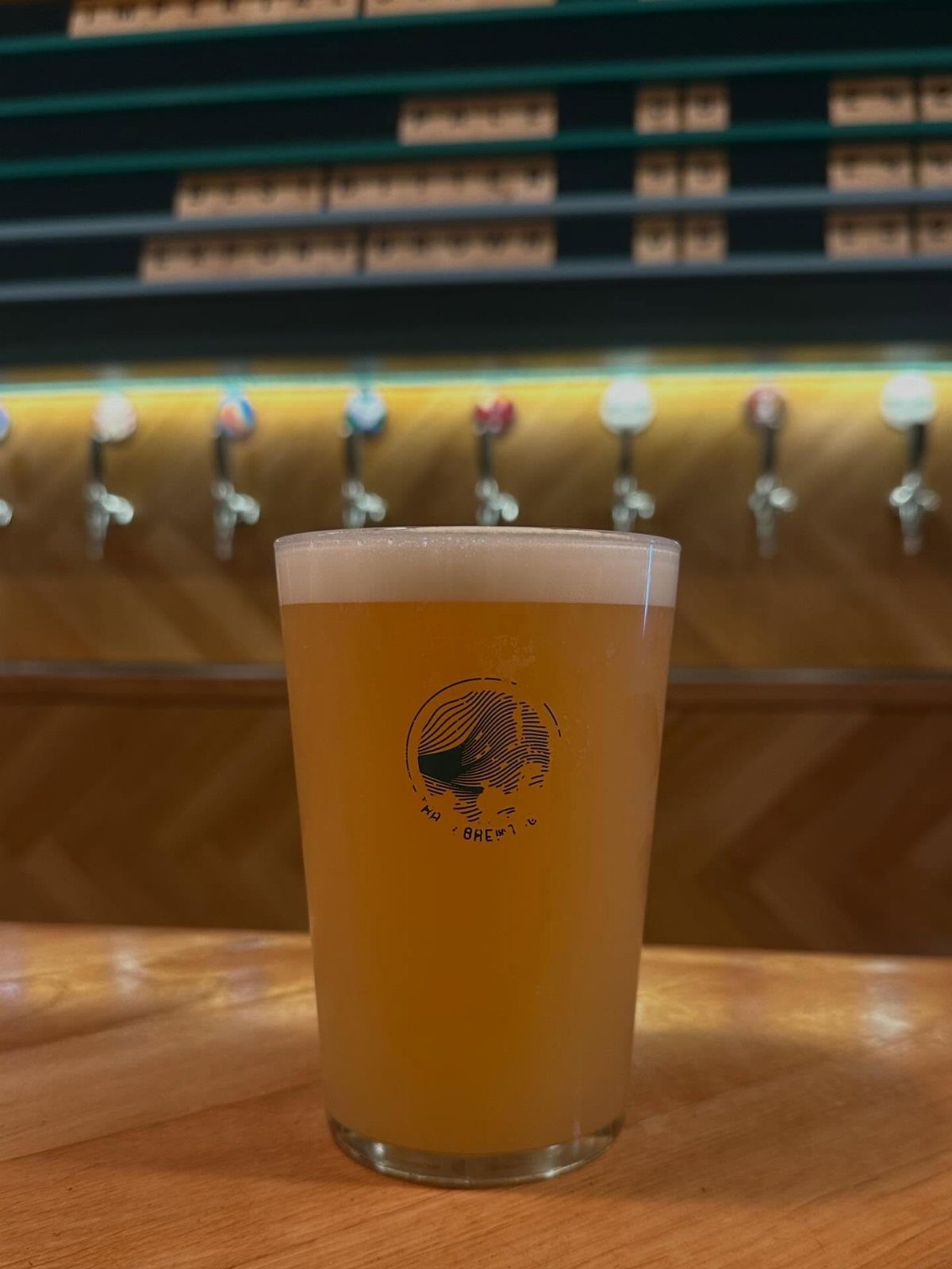 Glass of hazy golden beer on a wooden bar with taps behind it