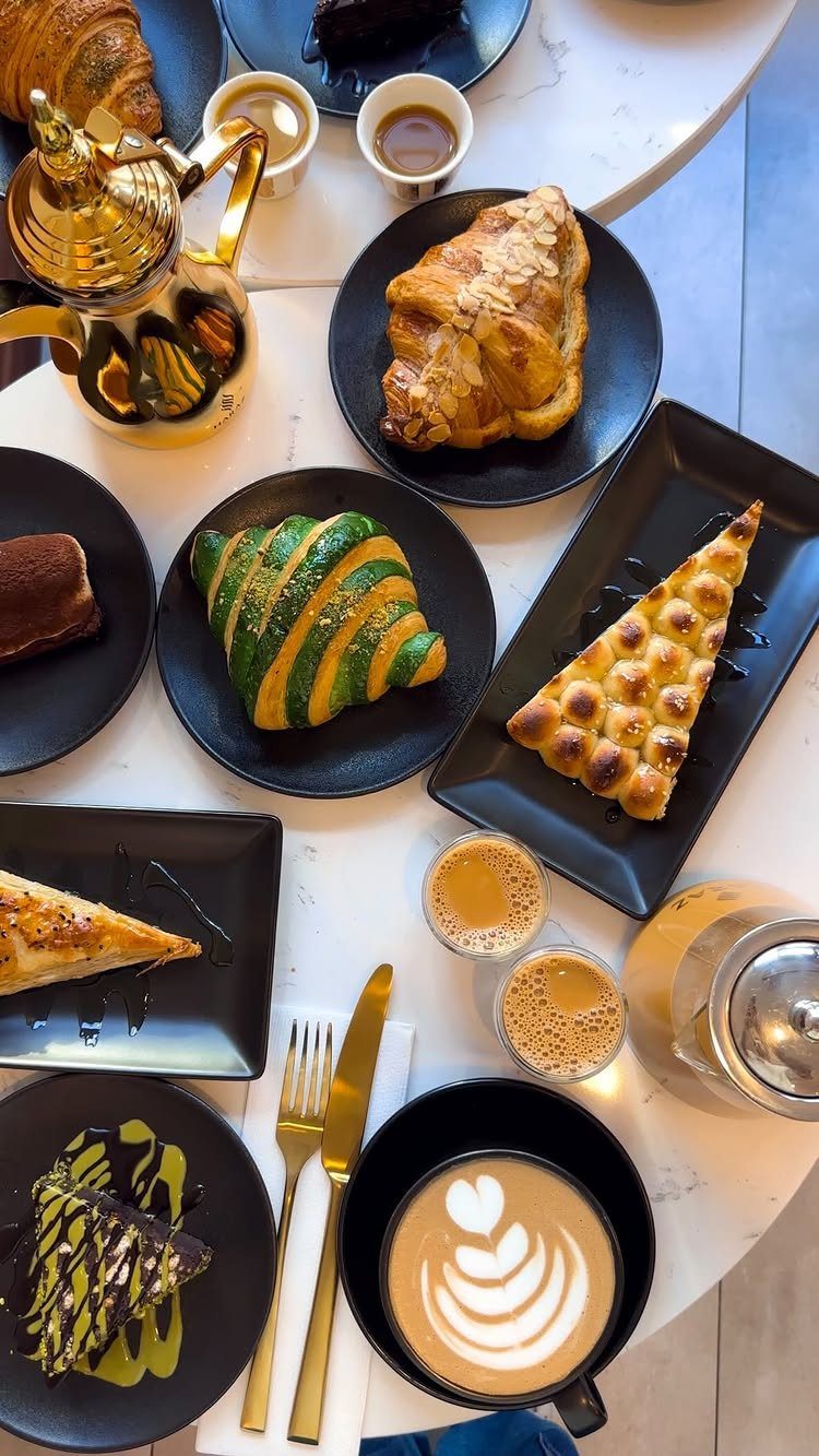 Assorted pastries and coffee drinks served on black plates on a marble table.