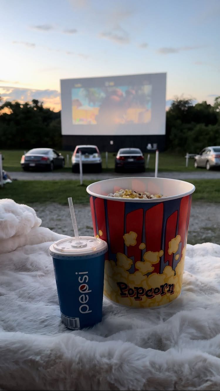Popcorn and soda on a fluffy blanket at an outdoor drive-in movie theater.