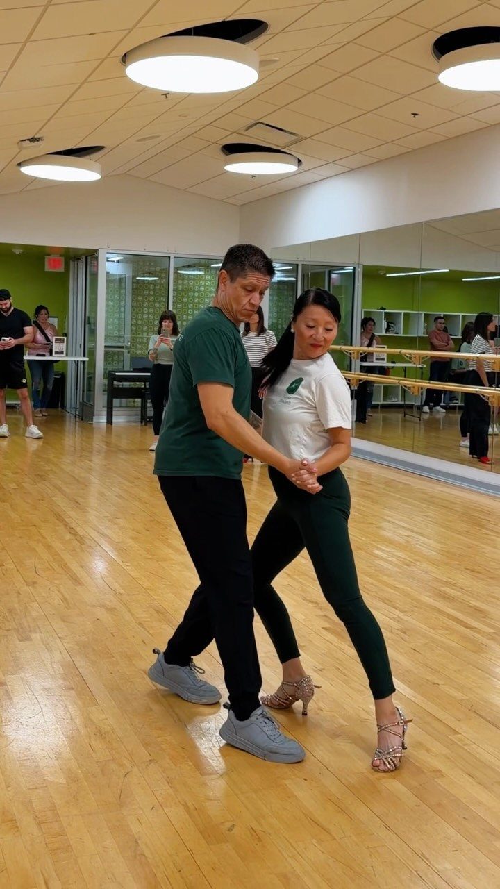 A couple dancing together in a bright studio with wooden floors and mirrors.