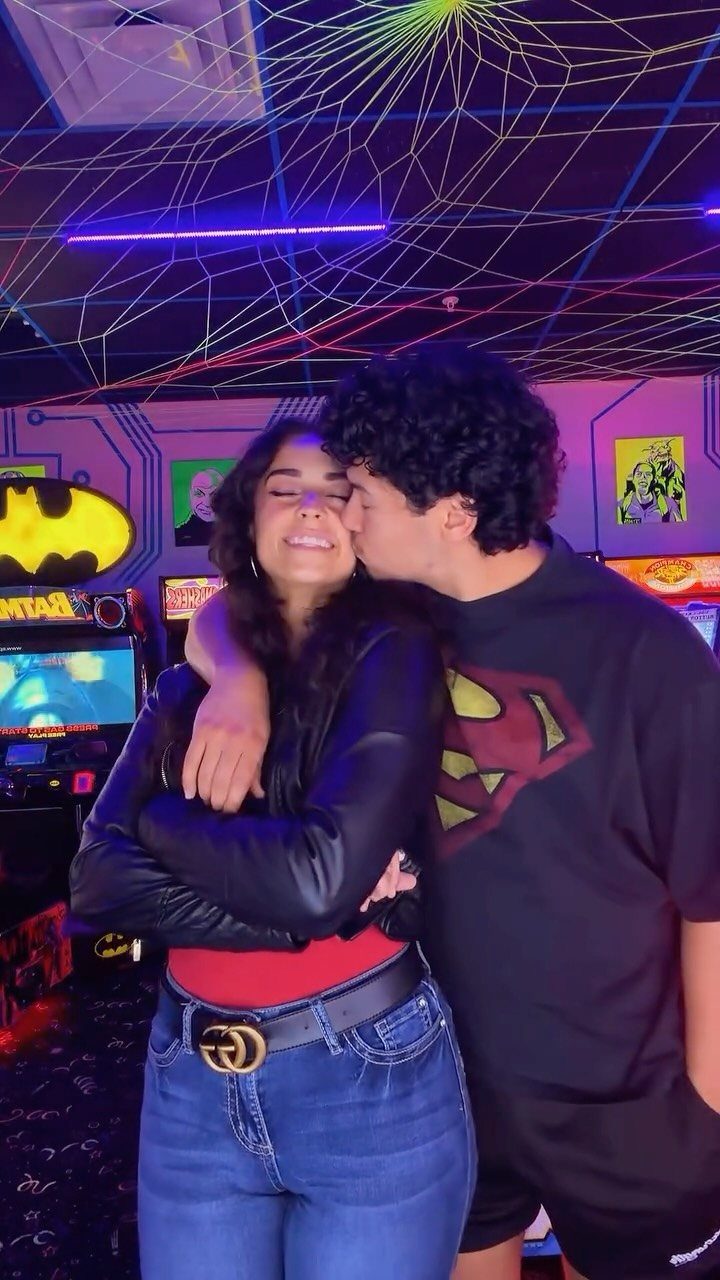 Young couple embracing and kissing in a neon-lit arcade with game machines.