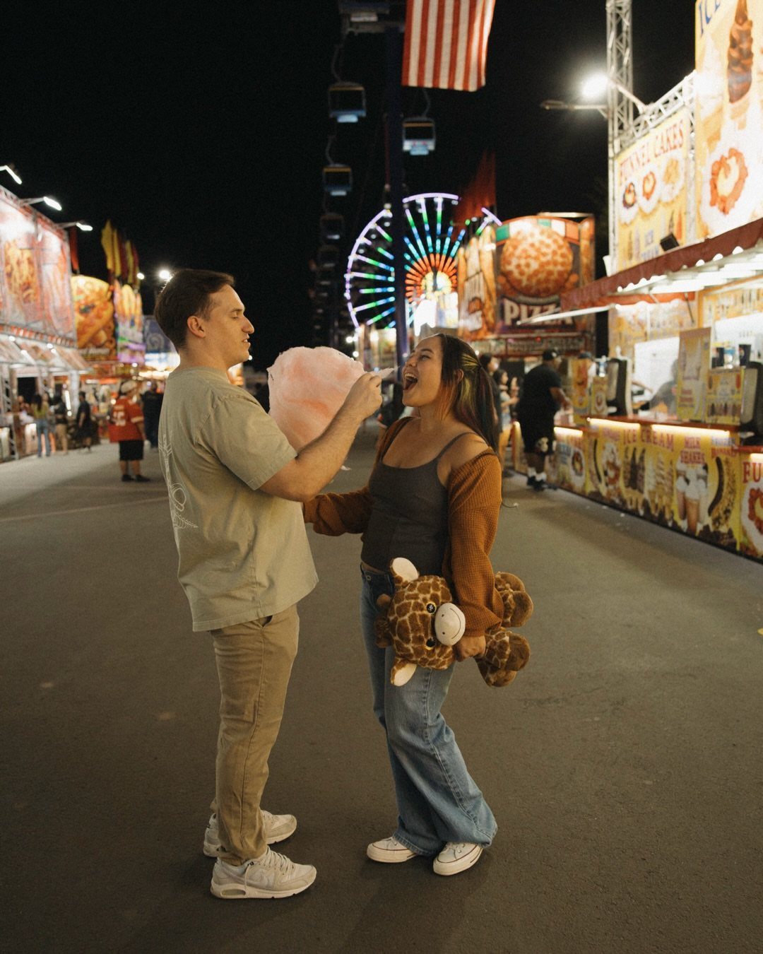 Couple eating cotton candy and holding a prize at a nighttime carnival fair.
